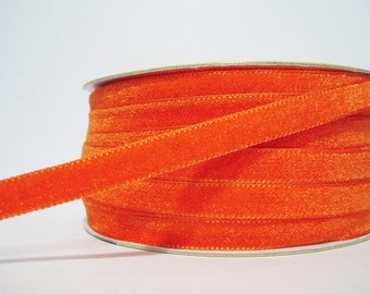 Könnte beinhalten: Eine Spule mit leuchtend orangefarbenem Samtband. Das Band ist weich und hat einen dezenten Glanz.