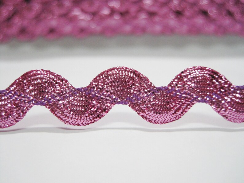 Peut inclure: Garniture m&eacute;tallique rose avec un bord ondul&eacute;. La garniture a un fil violet qui traverse le centre.