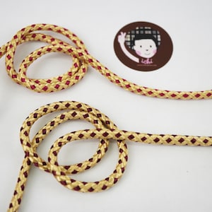 Op de afbeelding: Gouden en bordeaux gevlochten koord met een ruitpatroon. Het koord is gelust en geknoopt.