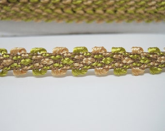 May include: A close-up of a beige and green braided trim with a repeating pattern. The trim is made of woven threads and has a slightly textured surface.