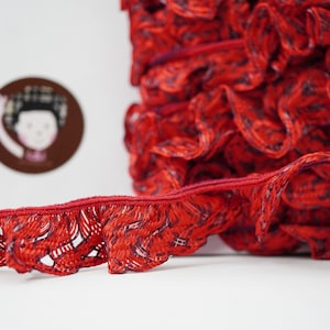 Könnte beinhalten: Roter Rüschenbesatz mit einem strukturierten Muster. Der Besatz ist aus einem weichen, flexiblen Material gefertigt und hat einen zarten, femininen Look.