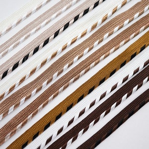 May include: Assortment of braided trim in various colours, including white, brown, beige, and gold. The trim has a white and black striped pattern.