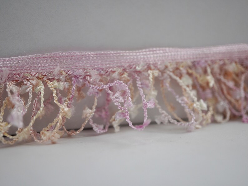 Puede incluir: Borde de flecos rosa y crema con un dise&ntilde;o delicado y texturizado. El fleco est&aacute; hecho de hilo suave y esponjoso y es perfecto para agregar un toque de elegancia a cualquier proyecto.