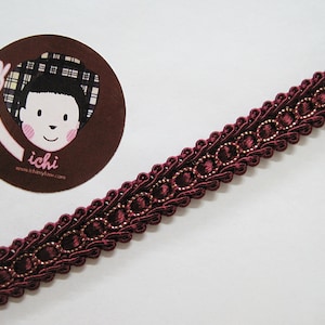 May include: Burgundy trim with gold accents. The trim has a repeating pattern of small circles and loops. The trim is approximately 1 inch wide.