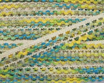 May include: A close-up of a beige crocheted trim with yellow, green, and blue accents. The trim has a scalloped edge and a textured design.
