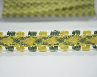 May include: Close-up of a decorative trim featuring a repeating pattern of yellow and green woven elements. The trim has a textured appearance and is likely used for embellishing clothing or craft projects. The color palette is soft and natural.
