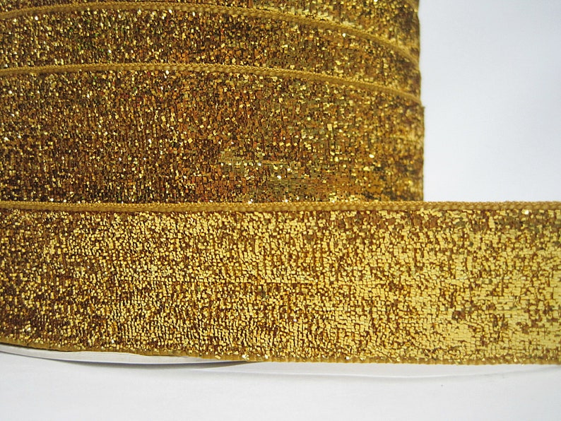 May include: Gold glitter ribbon with a textured surface. The ribbon is rolled up and the edges are visible.