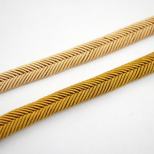 May include: Two pieces of braided trim, one in a light beige color and the other in a golden yellow color. Both trims have a herringbone pattern.