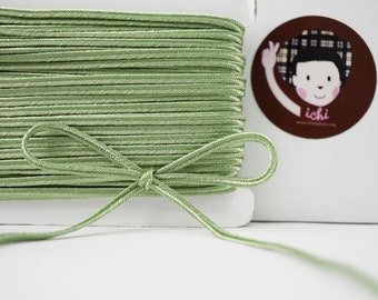 May include: A spool of pale green satin ribbon with a bow tied in the center. The ribbon is wound around a white cardboard spool.
