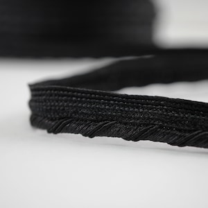 May include: Black trim with a decorative fringe. The trim is made of a woven fabric with a subtle texture.