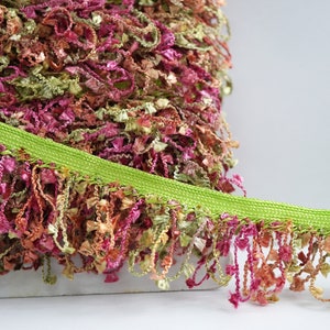 May include: A close-up of a green and multicoloured fringe trim. The fringe is made of a soft, fluffy material and has a subtle sheen. The trim is perfect for adding a touch of elegance to any project.