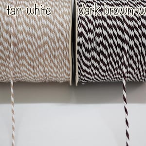 Puede incluir: Dos carretes de cuerda, uno beige y blanco, el otro marrón oscuro y blanco. La cuerda está bien enrollada en carretes de cartón. El texto "tan-white" y "dark brown-white" es visible en los carretes.
