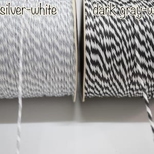Puede incluir: Dos carretes de hilo, uno plateado-blanco y otro gris oscuro-blanco. El hilo está enrollado firmemente en carretes de cartón. El texto "silver-white" y "dark gray-white" está escrito encima de cada carrete. Adecuado para manualidades y envolver regalos.
