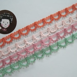 May include: Four different colours of scalloped lace trim. The colours are green, pink, light pink, and orange.