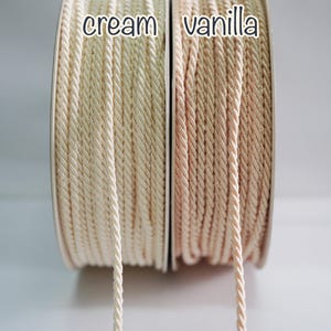 May include: Close-up of two spools of twisted cord in cream and vanilla colors. The cream cord is a light beige, while the vanilla cord is a soft, pale peach. The words "cream" and "vanilla" are printed above each cord.