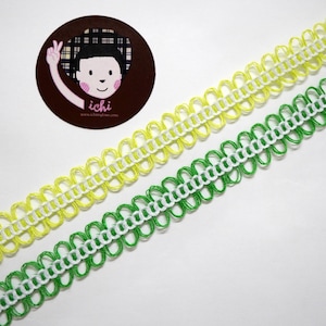 May include: Two decorative ribbons, one yellow and one green, with a white accent. The ribbons have a scalloped edge design. A circular sticker with a cartoon character and the text "ichi" is in the upper left corner.