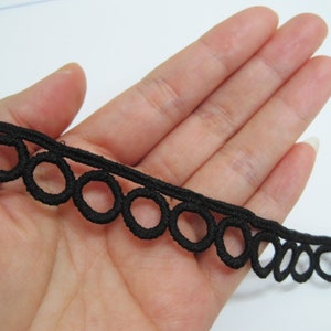 May include: Black elastic trim with a scalloped edge and a repeating pattern of small circles. The trim is approximately 1 inch wide.