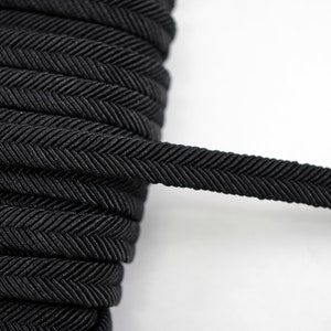 Puede incluir: Borde elástico negro de espiga. El borde está tejido con un patrón de espiga y tiene un acabado liso y ligeramente brillante.