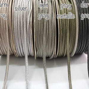 May include: Five spools of cord in different shades of gray. The spools are labeled "warm gray", "silver", "light gray", "gray metallic", and "dark gray".