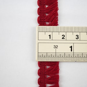 May include: Red fringe trim with a scalloped edge, measured against a ruler showing 1 inch.