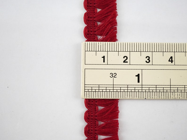May include: Red fringe trim with a scalloped edge, measured against a ruler showing 1 inch.