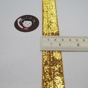 May include: Gold glitter ribbon measuring 1 inch wide. The ribbon is shown next to a ruler.