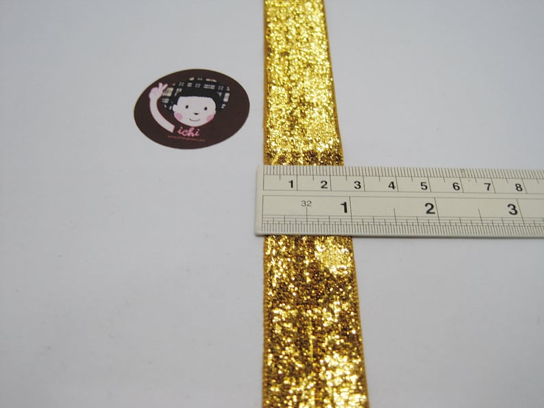May include: Gold glitter ribbon measuring 1 inch wide. The ribbon is shown next to a ruler.