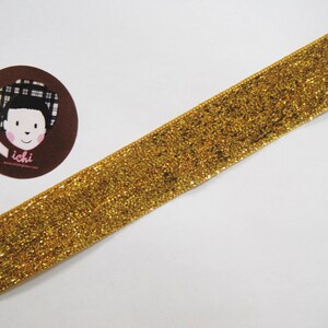 May include: Gold glitter ribbon with a subtle sheen. The ribbon is flat and has a smooth texture.