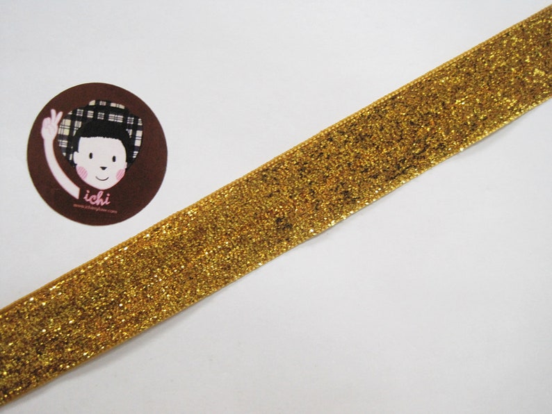 May include: Gold glitter ribbon with a subtle sheen. The ribbon is flat and has a smooth texture.