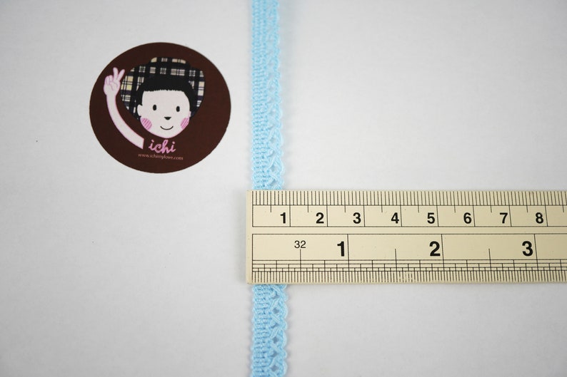 May include: A light blue lace trim measuring 1 inch (2.5 cm) in length. The trim is shown next to a ruler for size reference.