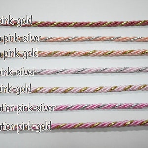 May include: Close-up of seven twisted cords in various shades of pink, with metallic accents. The cords are labeled with color combinations like "rose pink-gold" and "peach pink-silver". Ideal for crafting and jewelry making.