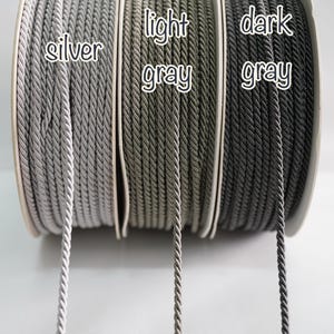 Może przedstawiać: Zbliżenie na trzy szpule skręconej liny w kolorze srebrnym, jasnoszarym i ciemnoszarym. Na szpulach widnieją napisy "silver", "light gray" i "dark gray". Lina jest ciasno nawinięta na szpule.