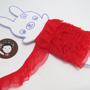 Puede incluir: Borde de encaje rojo con una textura delicada y transparente. El borde está doblado y se muestra en una tarjeta blanca con forma de conejo.