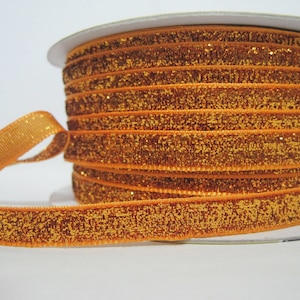 Könnte beinhalten: Eine Spule mit orangefarbenem Samtband mit goldenen Glitzer. Das Band ist um eine weiße Pappspule gewickelt.