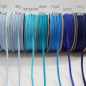 May include: A collection of ten spools of elastic cord in various shades of blue, from baby blue to deep navy. The spools are labelled with the colour names: baby blue, light blue, sky blue, turquoise, aqua blue, royal blue, azure, navy blue, and deep navy blue.