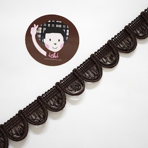 May include: Dark brown scalloped trim with a decorative design. The trim is made of a woven material and is displayed on a white background. A circular logo with a cartoon figure and the text "ichi" is in the upper left corner.