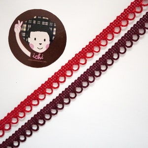 Op de afbeelding: Twee spoelen met rode en bordeauxrode elastische trim met een gegolfde rand. De trim is gemaakt van een zacht, rekbaar materiaal en is perfect om elke project een vleugje elegantie te geven.