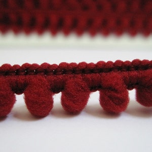 May include: Red pom-pom trim with a woven base. The trim is made of soft, fuzzy material and has a classic look.