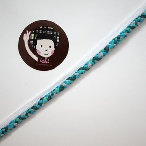 May include: A close-up shot features two cords: a white cord and a braided cord with teal, blue, and gray threads. A circular sticker with a cartoon illustration of a girl with the text "ichi" is in the upper left corner.