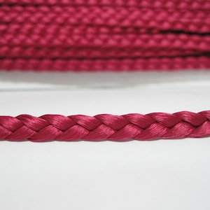 May include: A close-up of a deep pink braided cord. The cord is made of a soft, smooth material and has a subtle sheen.