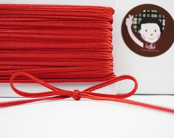 May include: A spool of red elastic cord with a bow tied in the cord. The cord is wound around a white card with the word "ichi" printed on it.