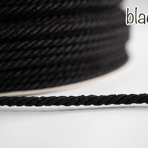 Puede incluir: Primer plano de una bobina de cuerda negra con textura trenzada. La palabra "black" está escrita a mano en la esquina superior derecha. La cuerda está bien enrollada y parece duradera.