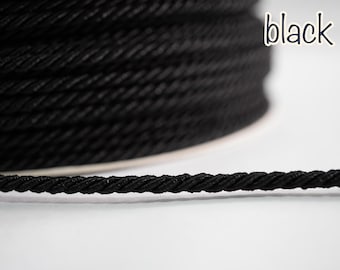May include: A spool of black rope with a twisted texture. The word "black" is written in a handwritten style in the upper right corner. The rope is tightly wound and appears durable.