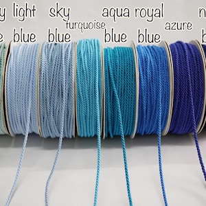 May include: Spools of blue cord in various shades, including baby blue, light blue, sky blue, turquoise, aqua blue, royal blue, azure, and navy blue. Each spool is labeled with its color name in white text.
