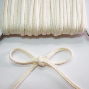 May include: A spool of off-white cotton cord with a bow tied in the cord.