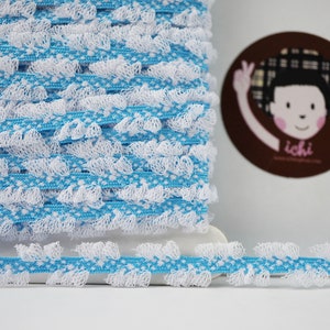 Op de afbeelding: Een rol blauwe en witte elastische trim met een gekrulde rand. De trim is gemaakt van een zacht, rekbaar materiaal en is perfect om een vleugje whimsy toe te voegen aan elk project.