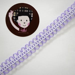 Puede incluir: Cinta decorativa con borde festoneado en lavanda y blanco. La cinta está colocada en diagonal. Una pegatina circular con una ilustración de dibujos animados y el texto "ichi" está en la esquina superior izquierda.
