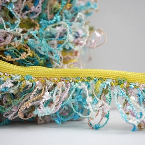 Puede incluir: Un ribete amarillo con una franja multicolor de azul, rosa, verde y blanco. La franja está hecha de un material suave y esponjoso.