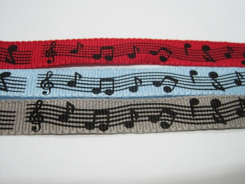 May include: Three different colored ribbons with a black musical note pattern. The ribbons are red, light blue, and gray.