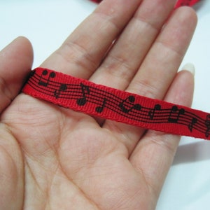 May include: Red ribbon with black musical notes printed on it. The ribbon is held in a hand.